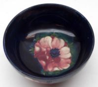 A shallow round Moorcroft Pedestal Bowl, decorated in an anemone pattern on a blue background, 6”