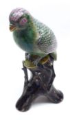 An Oriental Model of a perched parrot on a tree stump, the bird decorated predominantly in famille