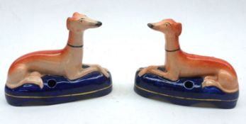 A pair of Staffordshire Inkwells, modelled as recumbent greyhounds decorated in orange and blues,