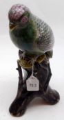 An Oriental Model of a perched parrot on a tree stump, the bird decorated predominantly in famille