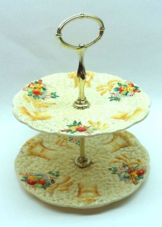 A Clarice Cliff Celtic Harvest Two Tier Cake Plate (dis-assembled), decorated with fruit and corn
