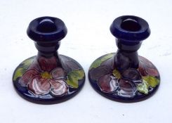 A pair of Moorcroft Candlesticks, decorated with the “Clematis” design on a dark blue ground,