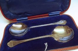 A Cased Pair of Edwardian Fruit Serving Spoons, Trefid and Rattail pattern with card cut circular