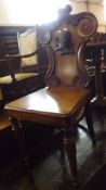 A Victorian Mahogany Hall Chair, the shaped back profusely carved with stylised foliage and centre
