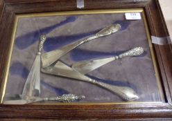 An Oak Surround and Glazed Frame holding five assorted steel bladed and silver handled Shoe Horns,