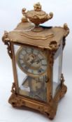 A late 19th/early 20th Century Four Glass Gilt Metal Cased Mantel Clock, crested with an urn finial,