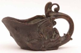 A Chinese Bronze Libation Cup, single scroll capped handle and the body embossed with Kaolin or