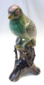 An Oriental Model of a perched parrot on a tree stump, the bird decorated predominantly in famille