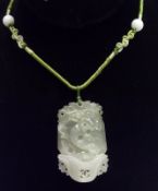 A carved and pierced Jadite Pendant mounted on a green woven fabric Necklet, the panel measuring
