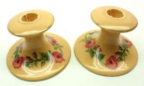 A pair of Clarice Cliff Newport Pottery small Squat Candlesticks decorated with garlands of roses on