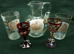 A small Clear Glass Ewer, decorated with a panel of cherubs; together with two matching Beakers