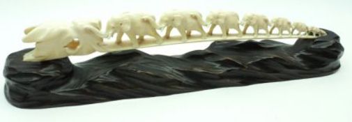 An Ivory Tusk carved in the form of a graduated line of elephants; together with matching hardwood