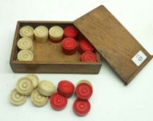 An Oak cased set of Ivory or Bone Draughts pieces of turned circular form, (16 white, 16 red),