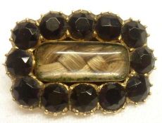 An early 19th Century Gold Mourning Brooch, featuring cut black stones surrounding a hair panel to