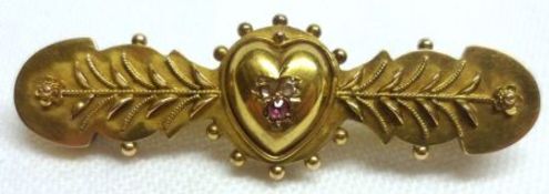 An Edwardian mid-grade precious metal Bar Brooch with applied foliate detail and stone set heart
