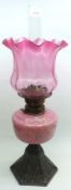 A late 19th Century Oil Lamp with crimped cranberry glass shade, pink opaque glass font decorated
