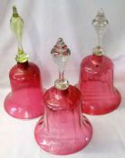 A collection of three Cranberry glass Bells, two with clear handles and one with a green handle,