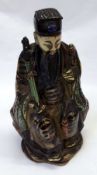 An unusual Oriental Pottery Figure of a seated Warrior with a sword in his left hand and its hilt