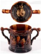 A large Staffordshire treacle glazed two-handled Loving Cup, the outer body embossed with panels