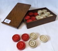 An Oak cased set of Ivory or Bone Draughts pieces of turned circular form, (16 white, 16 red),
