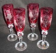 A set of four Bohemian style Champagne Flutes, all etched with foliage and berries on cranberry