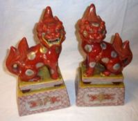 A pair of Kutani style Models of Temple Dogs perched on podiums, decorated predominantly in iron red