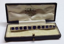A cased precious metal Long Bar Brooch, set with eleven graduated oval Blue Stones, interspersed