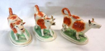 A collection of three Staffordshire Cow Creamers, all decorated in iron red and with gilded horns on
