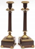 A pair of Lacquered and Patinated Brass Candlesticks, each with fixed nozzles over shallow drip pans