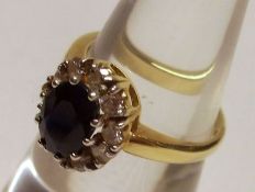 A hallmarked 18ct Gold centre Dark Blue Sapphire and ten small brilliant cut Diamond surround