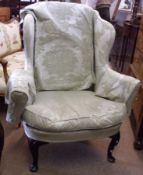 A Wing Armchair, with pale green floral print loose covers, raised on short cabriole front