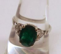 An unmarked precious metal Ring set with a facetted oval Emerald, having small Diamond mounts to the