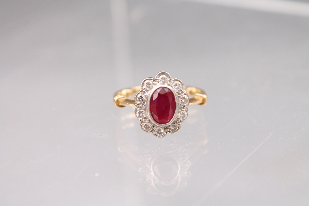 An 18ct gold ruby and diamond cluster ring, the centre oval ruby 7x5mm surrounded by 10 round