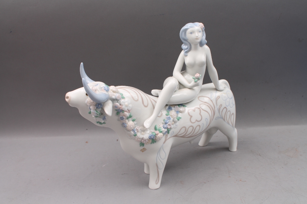 A Lladro figural group modelled as a young lady seated on a bull, 34cm long. This bull, modelled