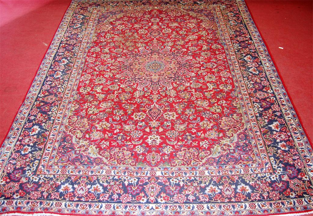 A Persian woollen red ground Tabriz carpet, decorated with a central medallion issuing scroll