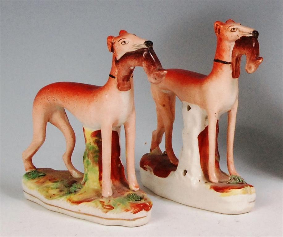 A pair of Victorian Staffordshire greyhounds, with dead hares in their mouths, each raised on oval