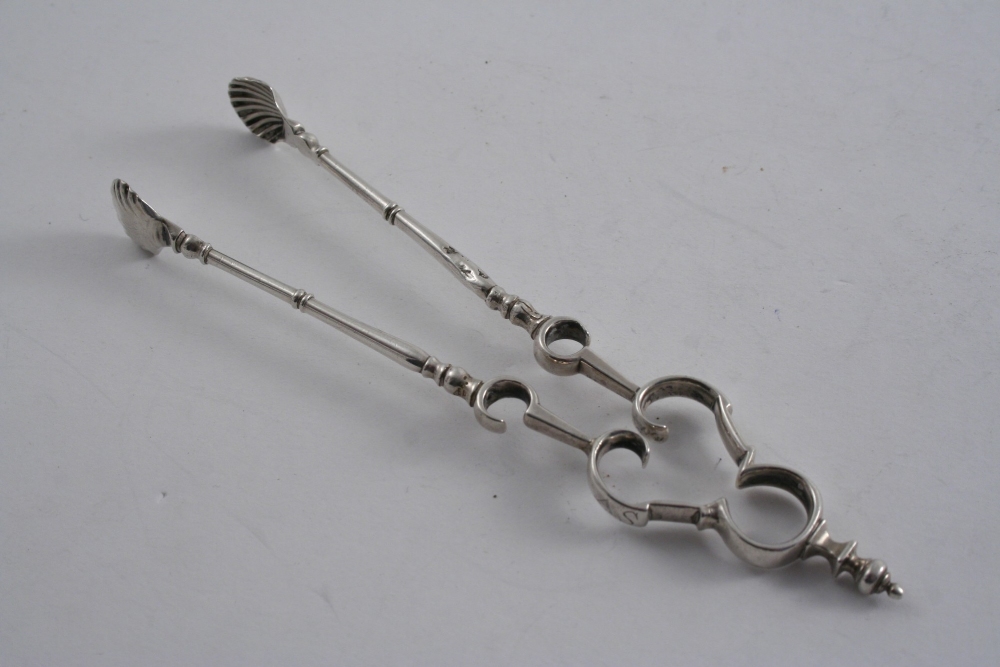 A PAIR OF EARLY 18TH CENTURY "ANDIRON" SUGAR TONGS with shell bowls & a knop finial, scratched