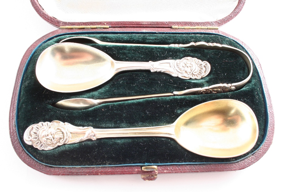 A CASED VICTORIAN PARCELGILT CADDY SPOON, SUGAR SPOON & A PAIR OF SUGAR TONGS with a jovial mask