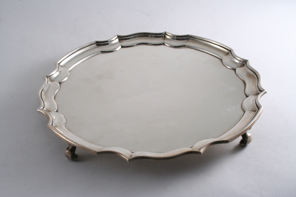 A MODERN SALVER of shaped circular outline with a moulded border & scroll feet, the reverse with a