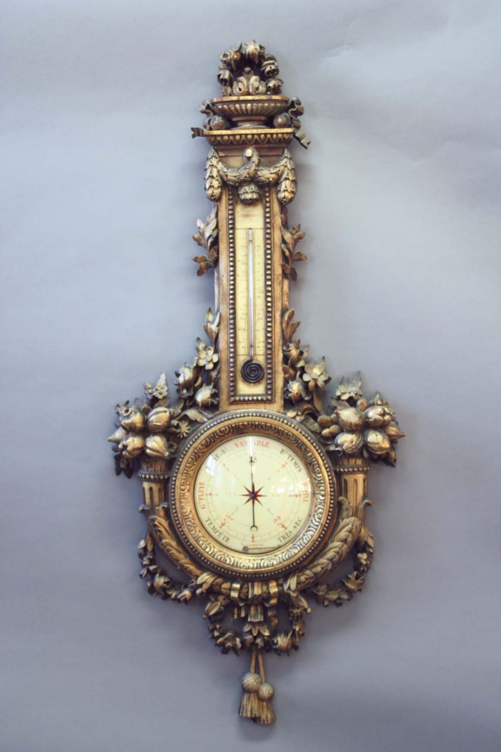 A LOUIS XVI STYLE GILTWOOD BAROMETER with a painted dial and scrolled alcohol thermometer, the