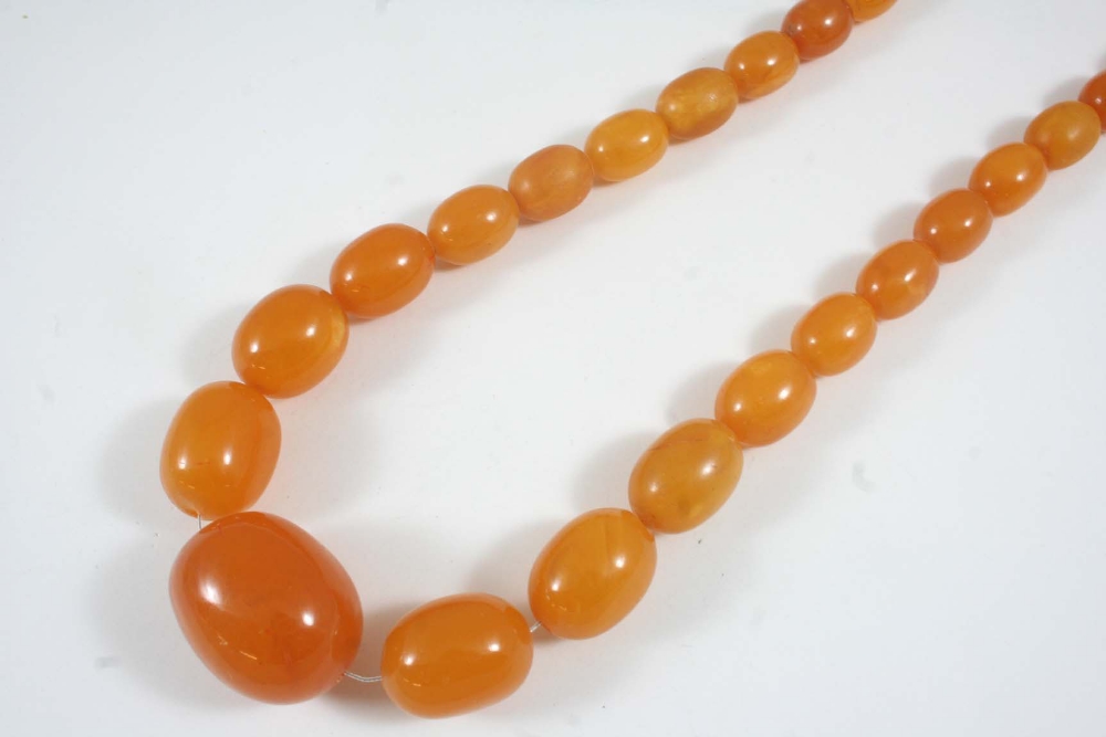 A GRADUATED AMBER BEAD NECKLACE formed with oval-shaped amber beads, 68cm. long, 84 grams.