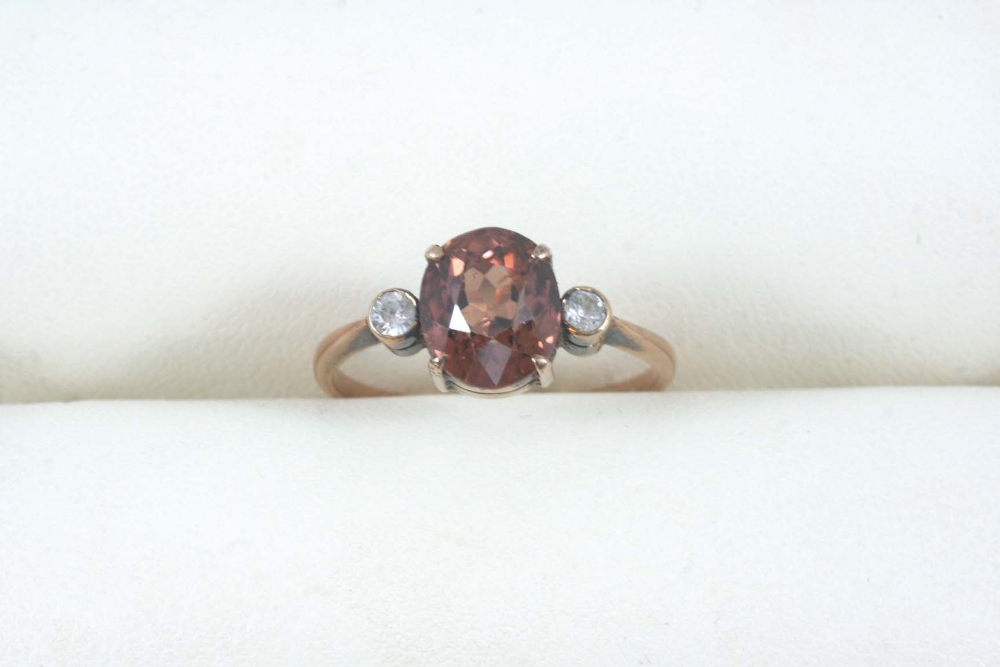 A GEM SET THREE STONE RING set with an oval-shaped zircon and two circular white stones, in gold.