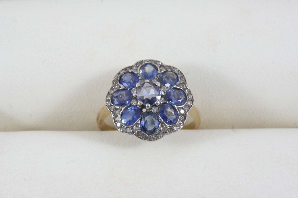 A SAPPHIRE AND DIAMOND CLUSTER RING of flowerhead form, set with a circular-cut sapphire within a