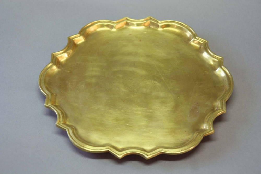 A BRASS SALVER of silver shape with bath border, on three bracket feet, 10ins. (26cms.) dia.