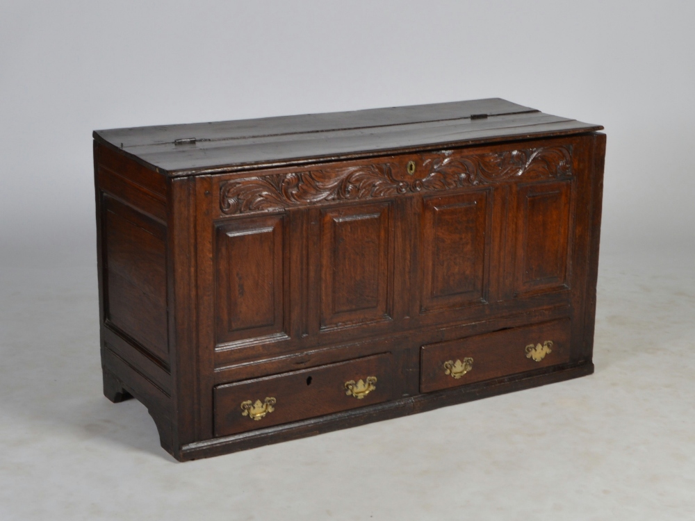 An 18th century and later stained oak coffer, the hinged plank top above a later carved acanthus