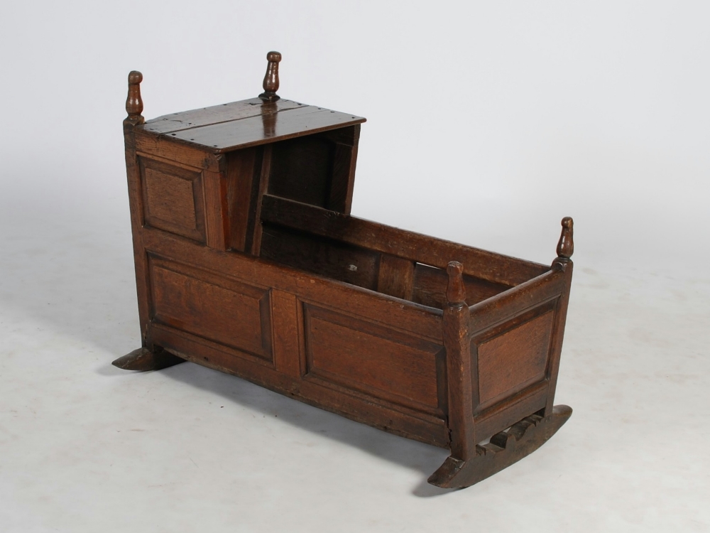 An 18th century stained oak cradle, constructed on panelled form, 90cm long x 72.5cm high x 53.5cm