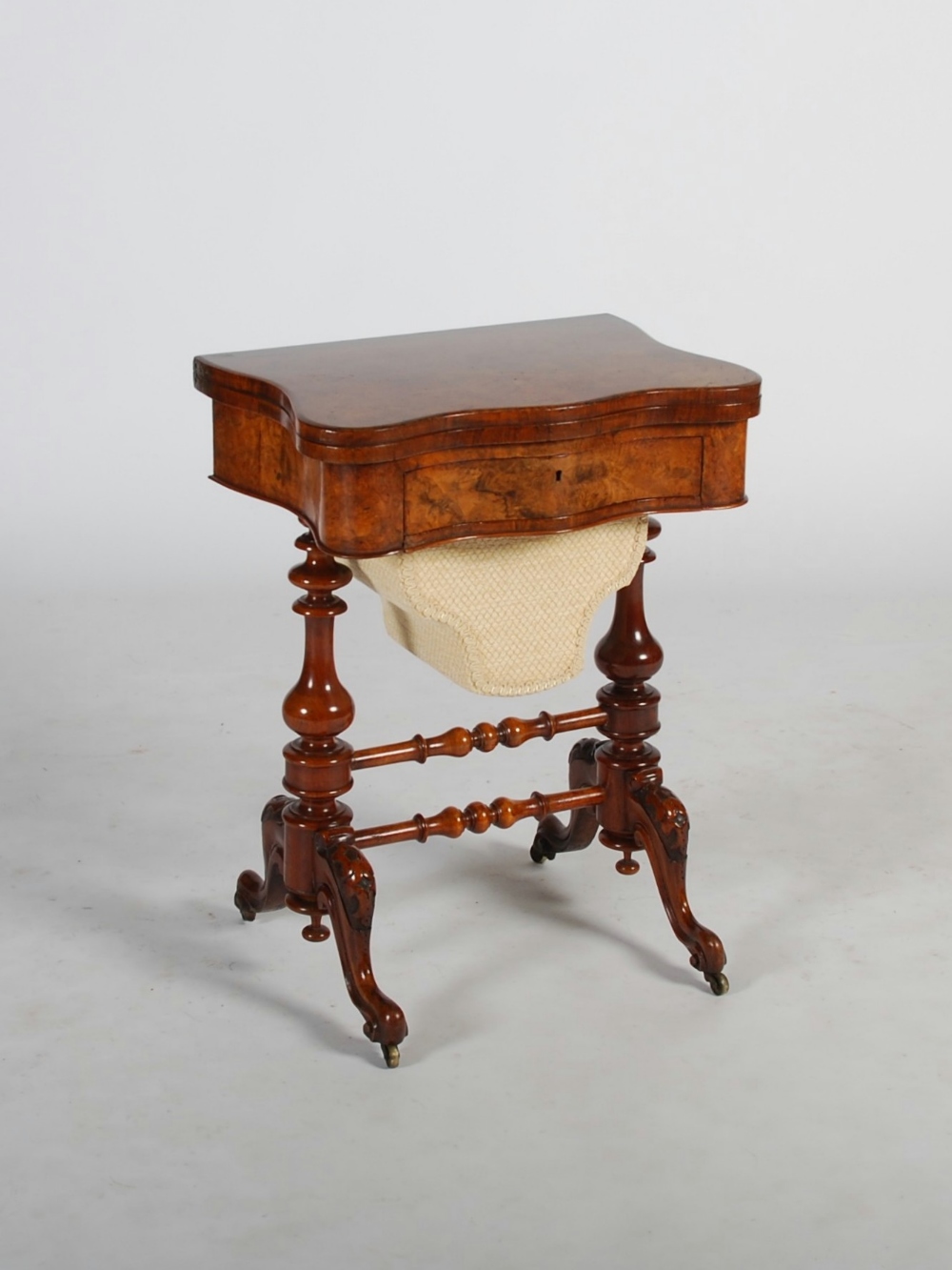 A Victorian walnut serpentine games/ work table, the hinged revolving top opening to reveal three