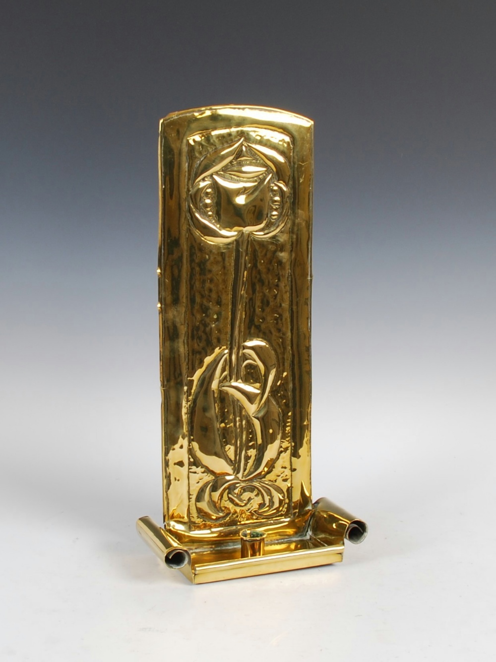 A Glasgow School brass wall sconce, with embossed decoration of rose and foliage, the scroll ended