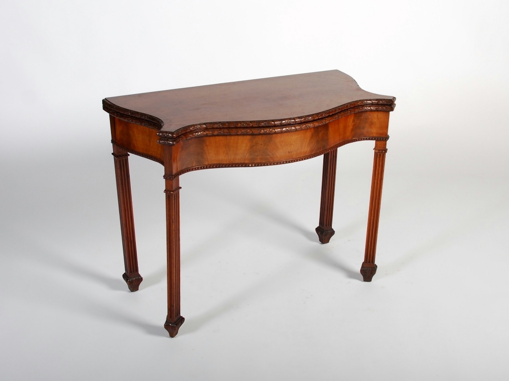 A George III style mahogany serpentine card table, the shaped top with a foliate carved edge opening