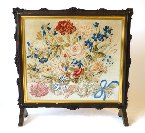 An Edwardian stained gesso framed tapestry fire screen with floral tapestry insert under glass on